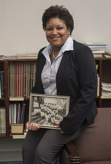 Neal Monique sitting in front of a bookshelf, holding a black and white photo.