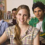 High school student smiling in a classroom with peers sitting behind her.