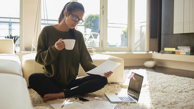 woman sitting on floor with laptop drinking coffee with legs crossed