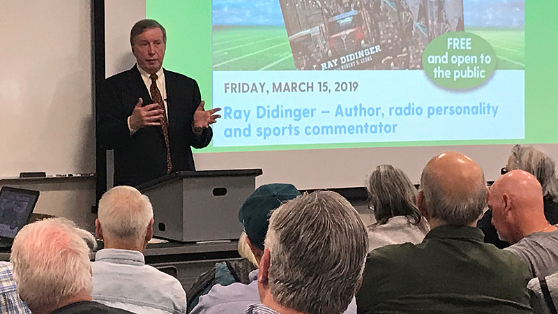 Ray Didinger extending arms while speaking in front of crowded room