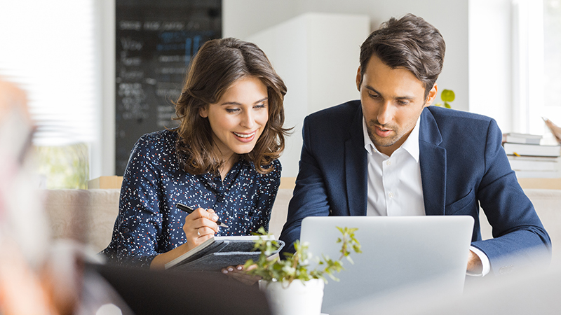 Woman taking notes while man works on laptop