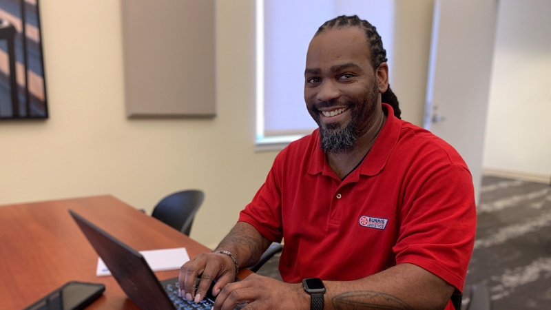 James Maynard looks up with a smile while working on laptop