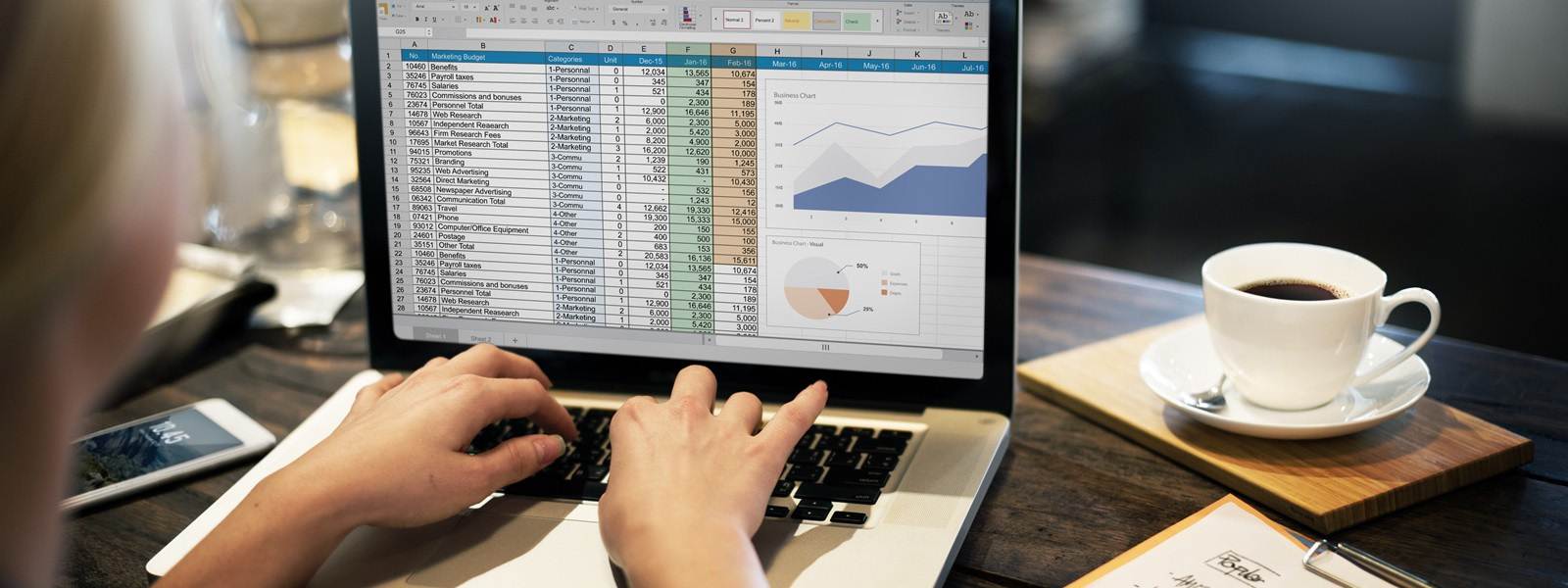 Two hands on laptop with Excel table on screen and cup of coffee to the right