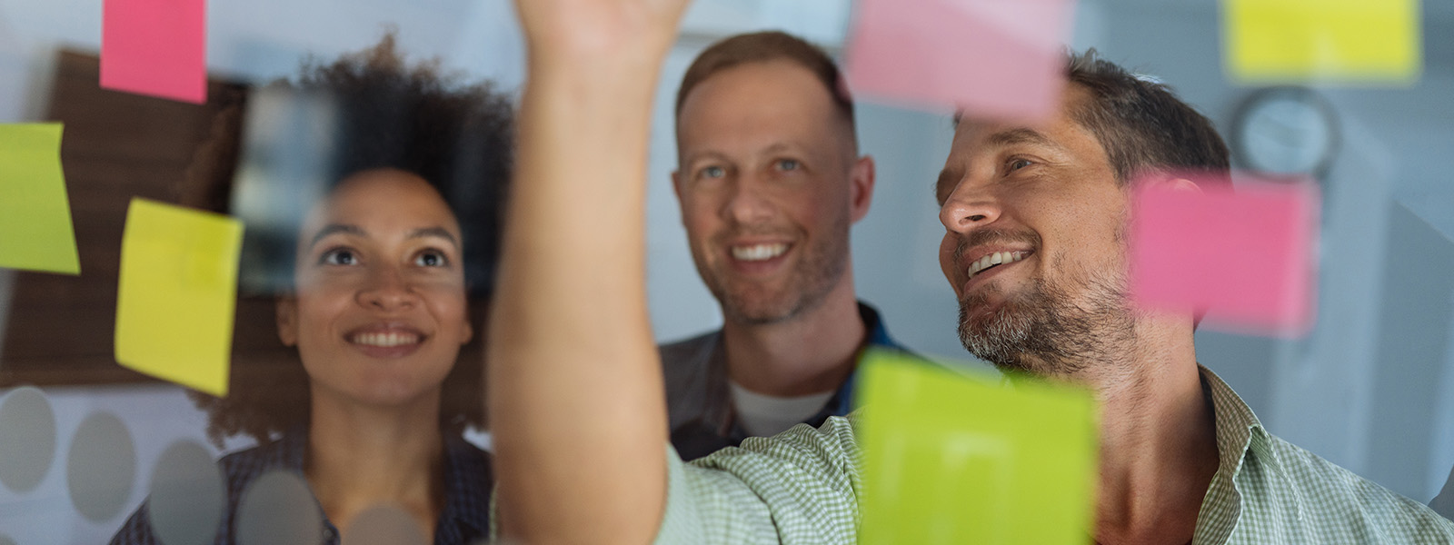 One woman and two men looking at sticky notes on glass wall