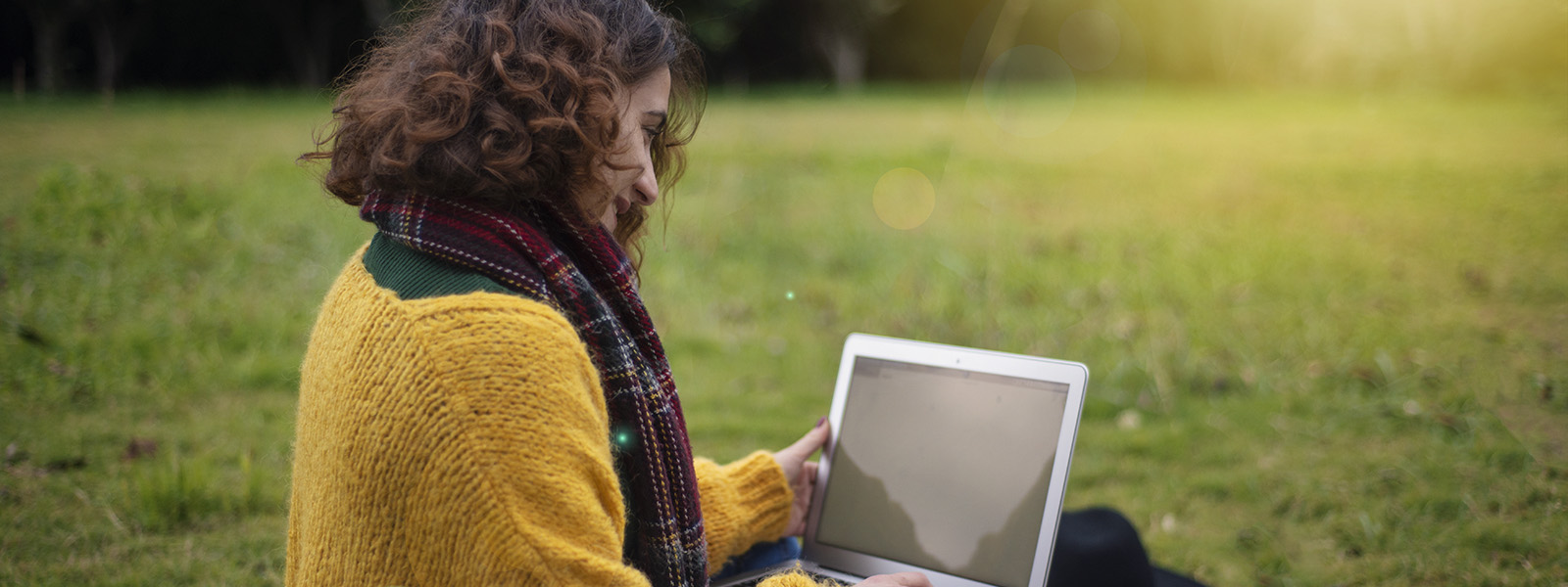 Young woman sitting on grass working on laptop