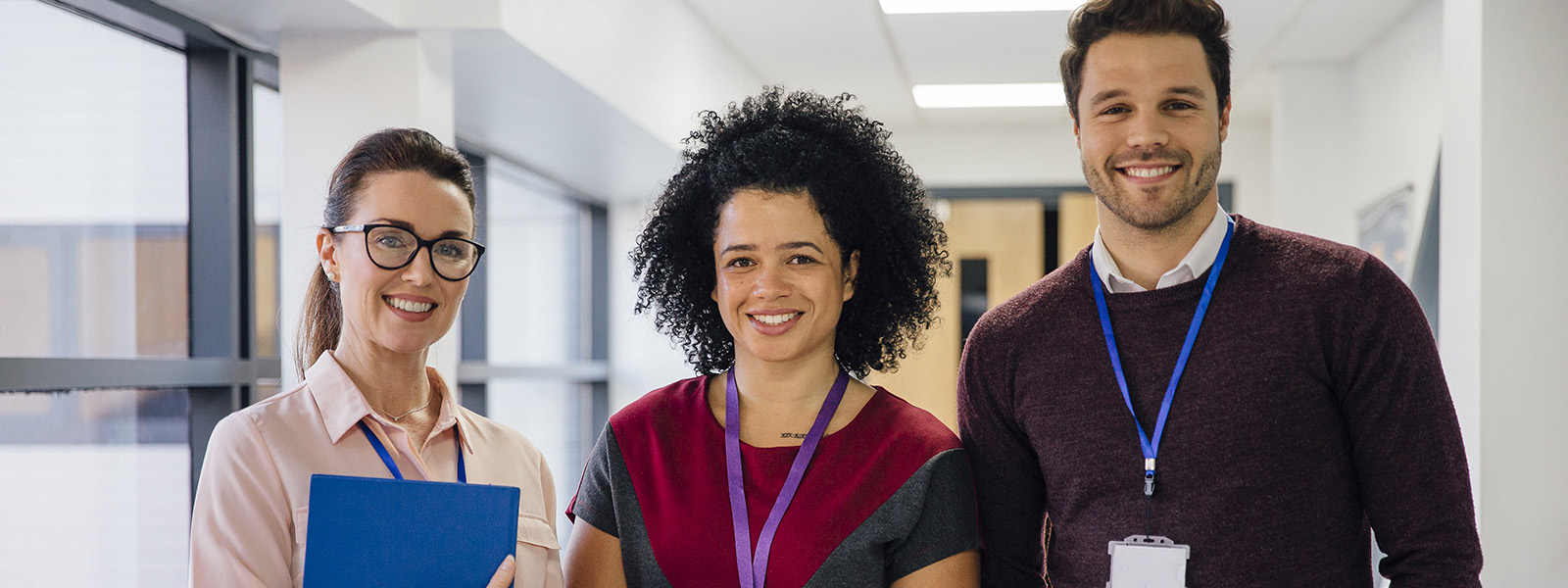 two female teachers and one male teacher standing together in a school hallway