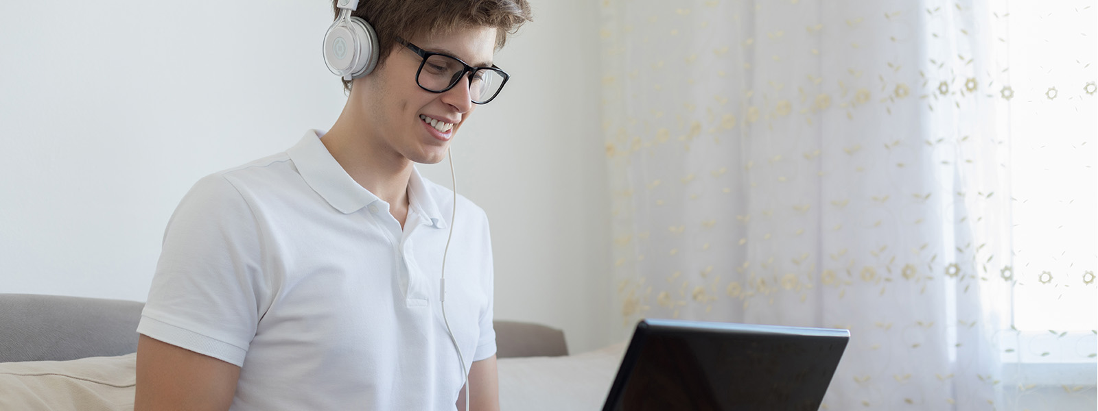 teenage boy on couch wearing headphones working on laptop