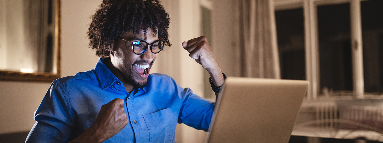 Male student working at home on laptop cheering