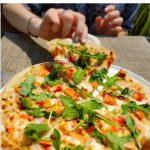 Facebook post of woman's right hand taking a slice of pizza from a full pie