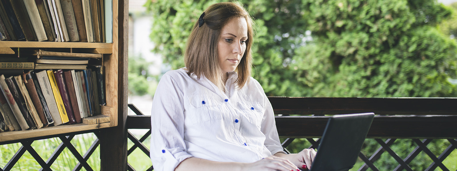 Woman working on laptop next to bookcase with trees in background