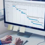 Male working on schedule on large computer monitor next to window