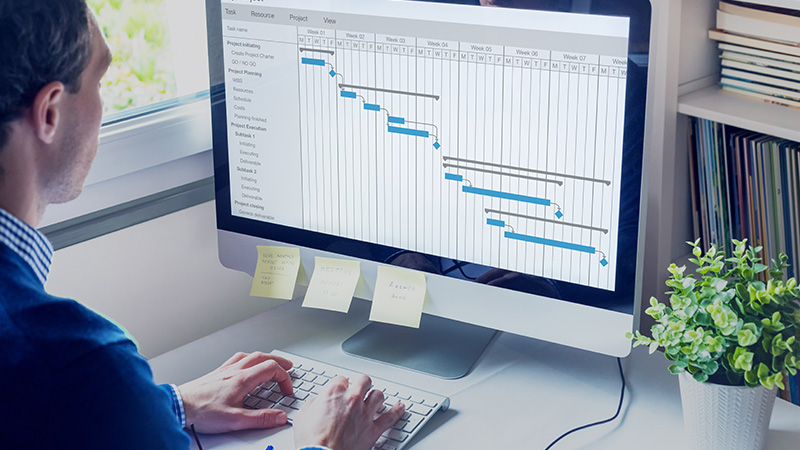 Male working on schedule on large computer monitor next to window