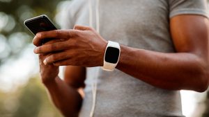 male athlete wearing fitness tracker on left wrist using smartphone with both hands