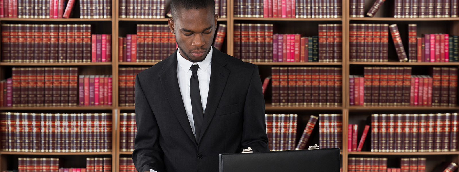 Young male lawyer in suit standing in library with shelves of law books behind him