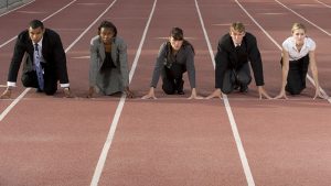 Five adults in business attire ready to run a race on a track