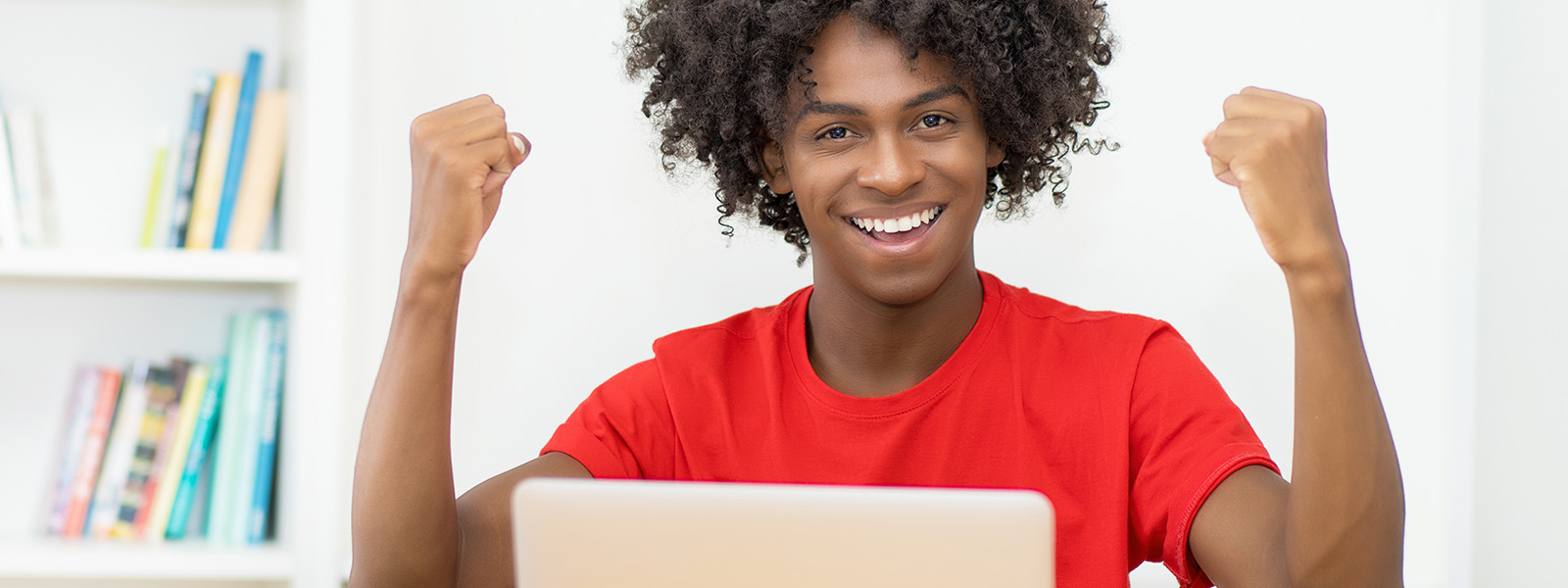 High school student sitting laptop raising two fists in celebration