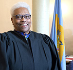 Paralegal graduate Carmen Jordan Cox in magistrate gown in front of Delaware flag