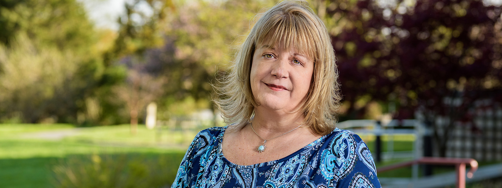 Paralegal graduate Sandra Kece posing outdoors in front of trees and grass