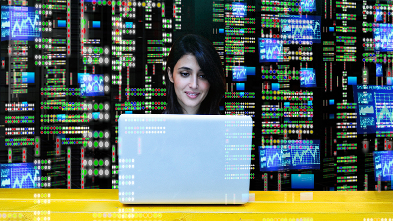 Woman on laptop with wall of data behind her