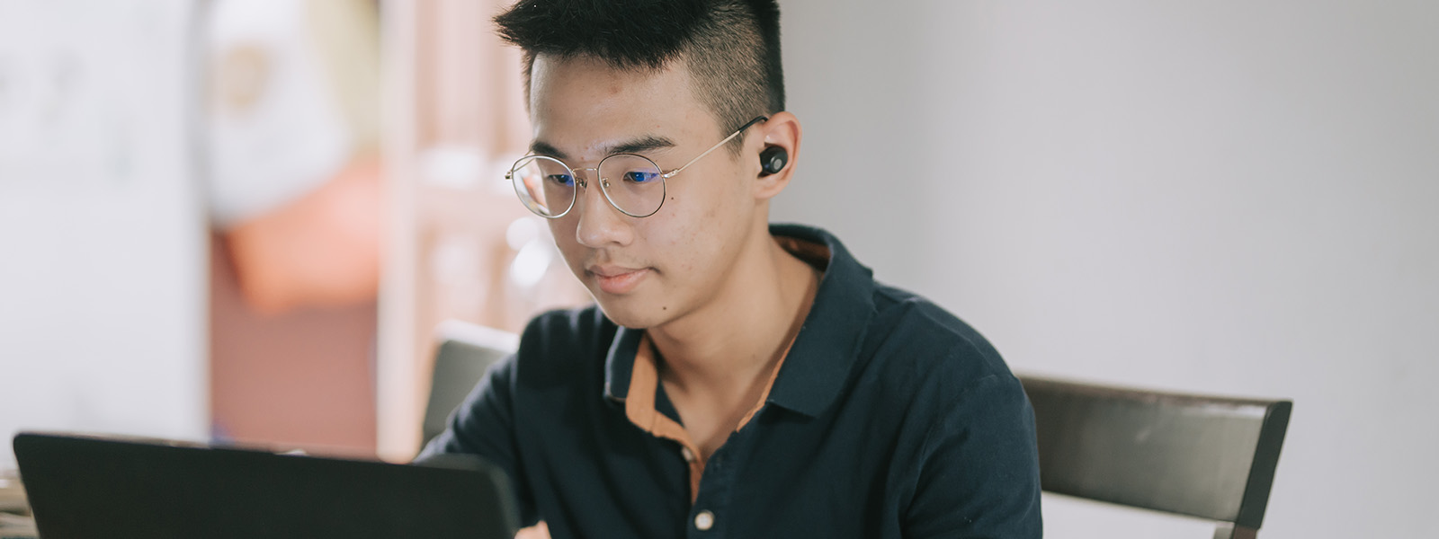 Male teenage sitting at kitchen table working on laptop
