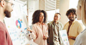 Young businesswoman is standing and explaining charts to her colleagues during a meeting in the office.