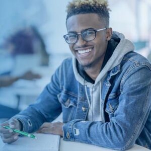 Young man writing in notebook at a table, smiling.