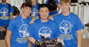 Three students hold a robotic vehicle as they participate in the Autonomous Driving Academy