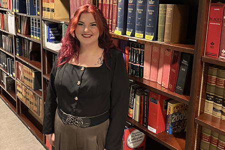 Paralegal pictured in a library with books and shelves in the background