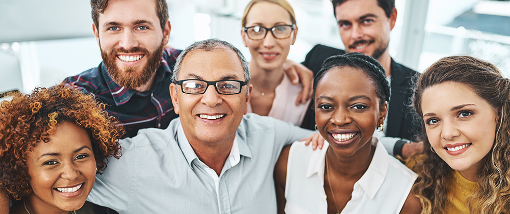 Six adults of varying ages pose together in a bright office environment, representing collaboration, learning, and professional development.